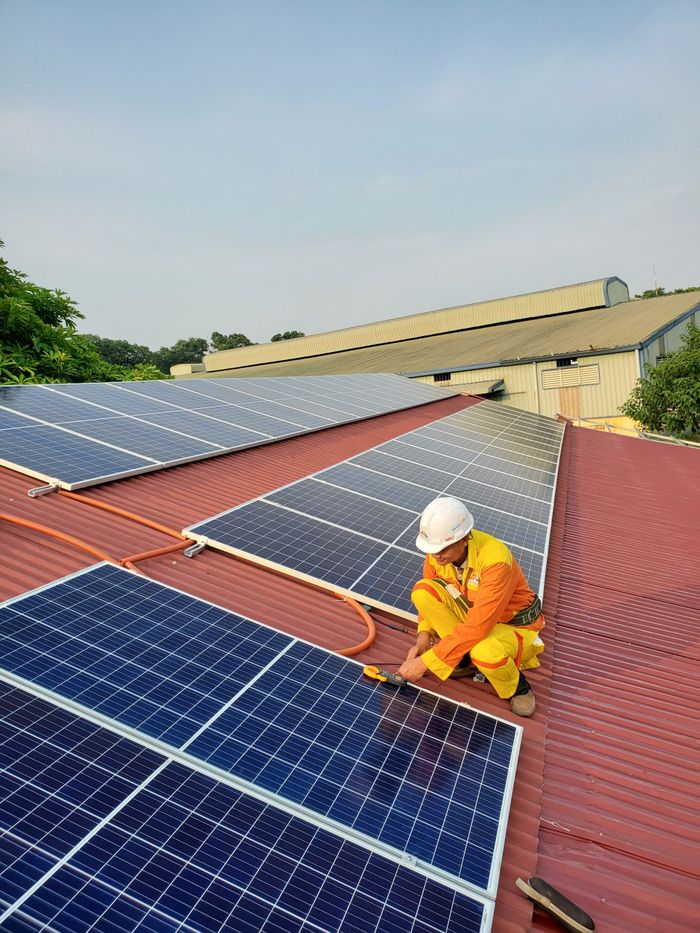 Technician working on solar panel installation on a rooftop under clear sky.