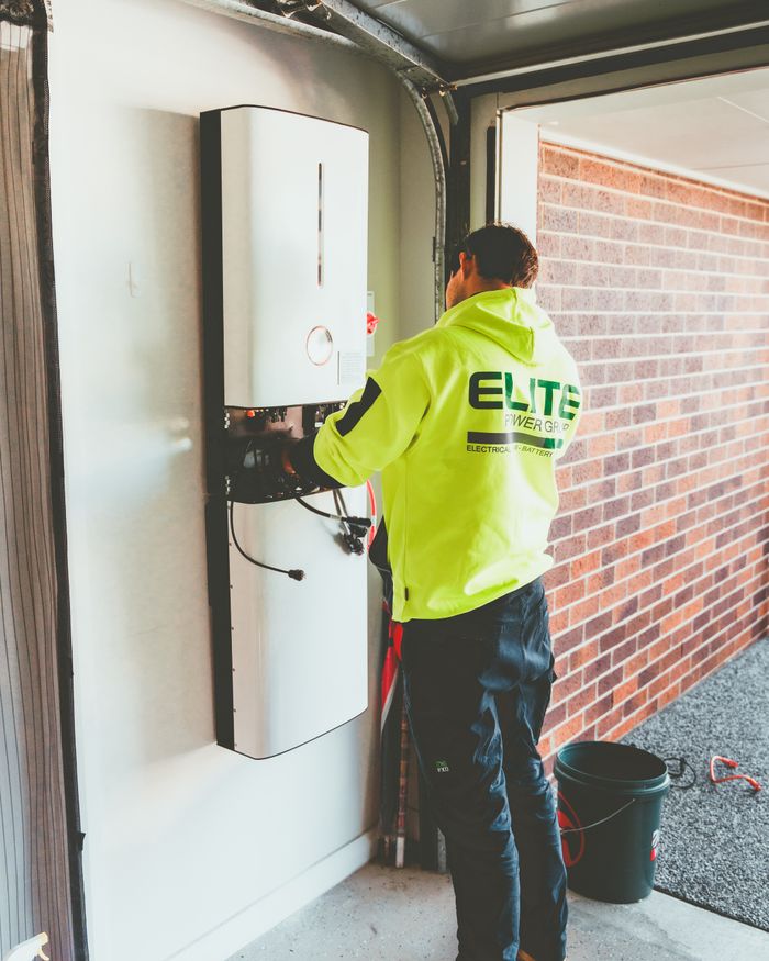 Electrician working on a solar inverter installation inside a garage in New South Wales, Australia.