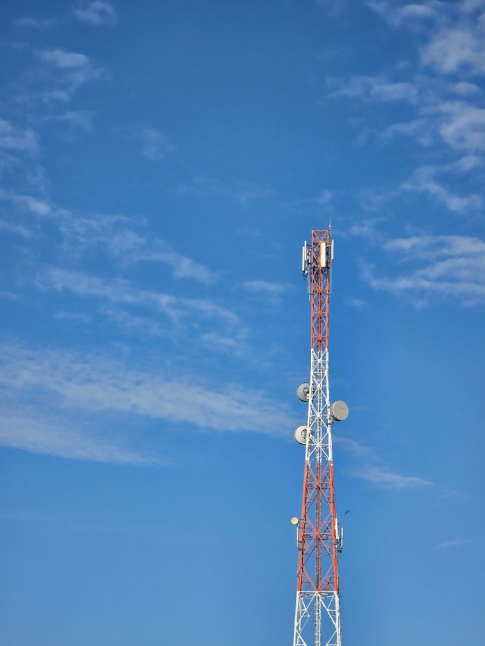 Red and white communication tower against a blue sky with scattered clouds.