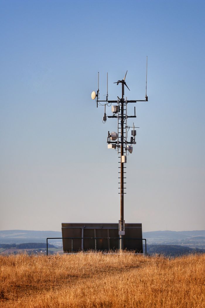 A solitary communication tower standing in a rural field under a clear blue sky.