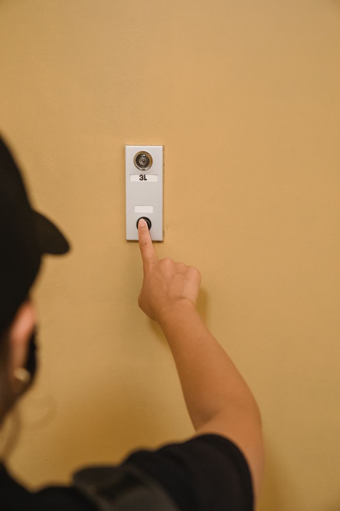 Close-up of a person pressing a doorbell on a beige wall, emphasizing hand action.